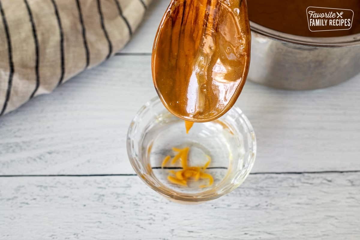 Dripping caramel into a small glass of water from a wooden spoon.