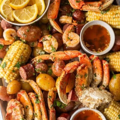 Sheet pan with crab legs, shrimp, potatoes, sausage, corn, butter and lemon wedges.
