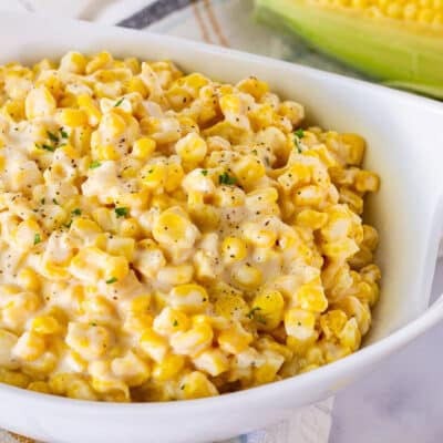 Bowl of Creamed Corn garnished with fresh parsley, salt and pepper. Fresh corn in the background.