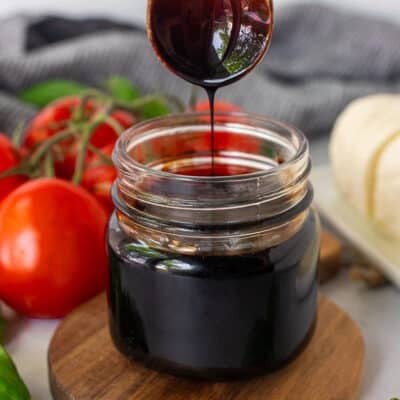 Jar of Balsamic Glaze and balsamic glaze drizzling from a wooden spoon.