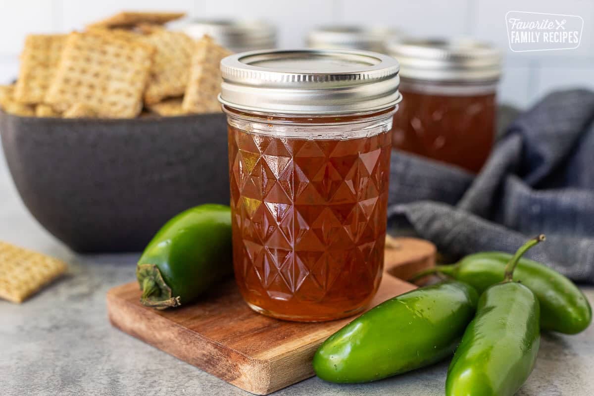 Jalapeño pepper jelly in a jar next to fresh jalapeños. Crackers in the background.