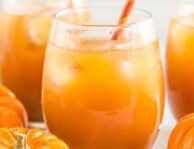 A glass of pumpkin juice with ice and a straw