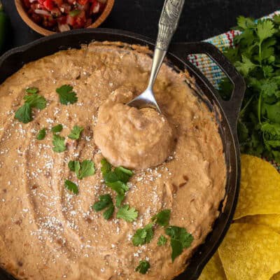 Skillet of Cheater Refried Beans with cilantro and cojita cheese. Spoon resting in the skillet.
