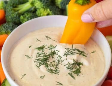 Dipping a yellow bell pepper into a bowl of veggie dip.