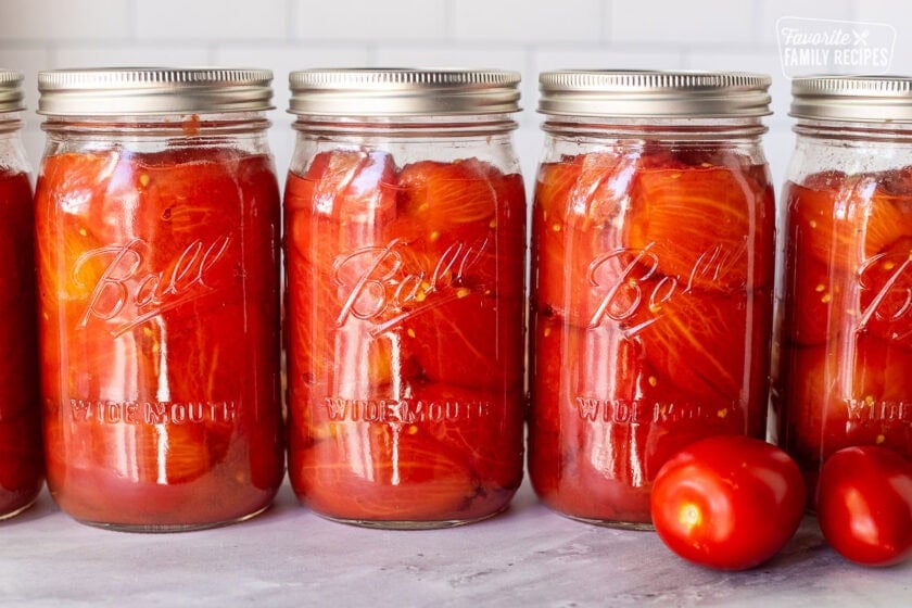 Lined up canning jars with whole tomatoes.