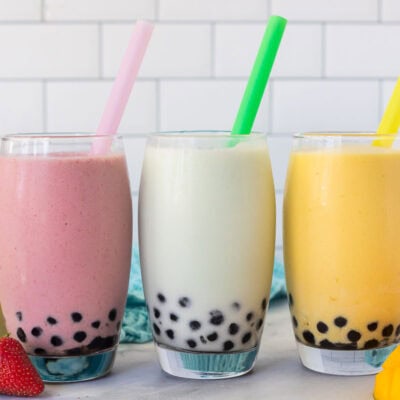 Strawberry, honeydew melon and mango boba smoothies in glasses with colorful large straws.