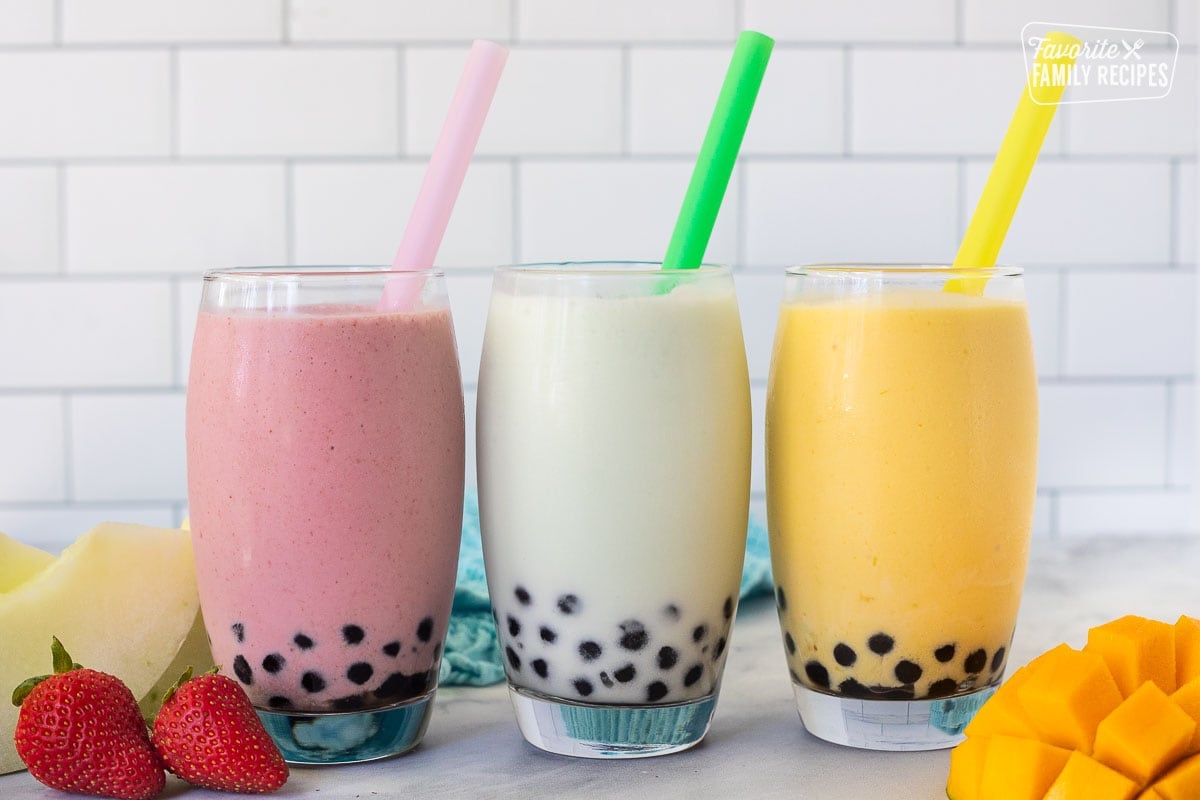 Strawberry, honeydew melon and mango boba smoothies in glasses with colorful large straws.