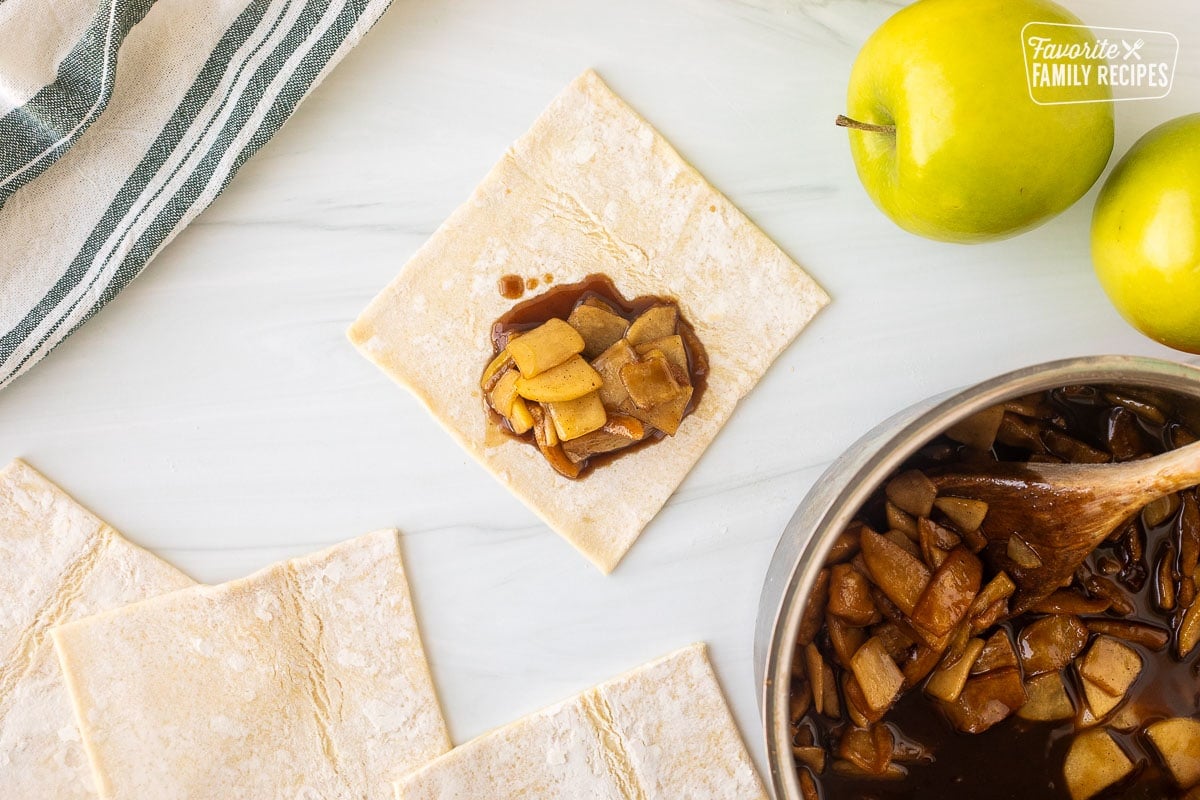 Puff pastry square with apple filling next to saucepan of cooked apples.