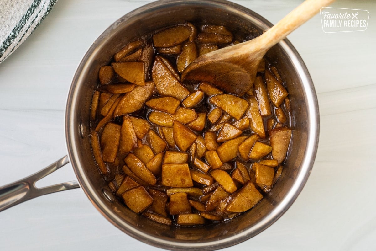 Cooked apples in a saucepan with a wooden spoon.