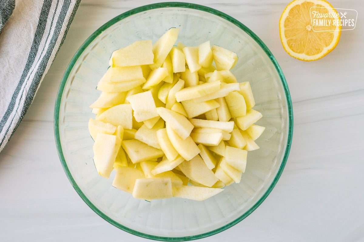 Glass bowl with cut up apple pieces. Lemon juice on the side.