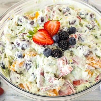 Glass mixing bowl with Easy Fruit Salad with Cool Whip topped with strawberry, blackberries and blueberries.