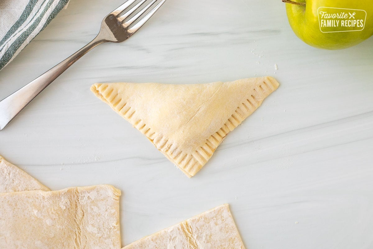 Folded over apple turnover with crimped edges. Fork on the side.