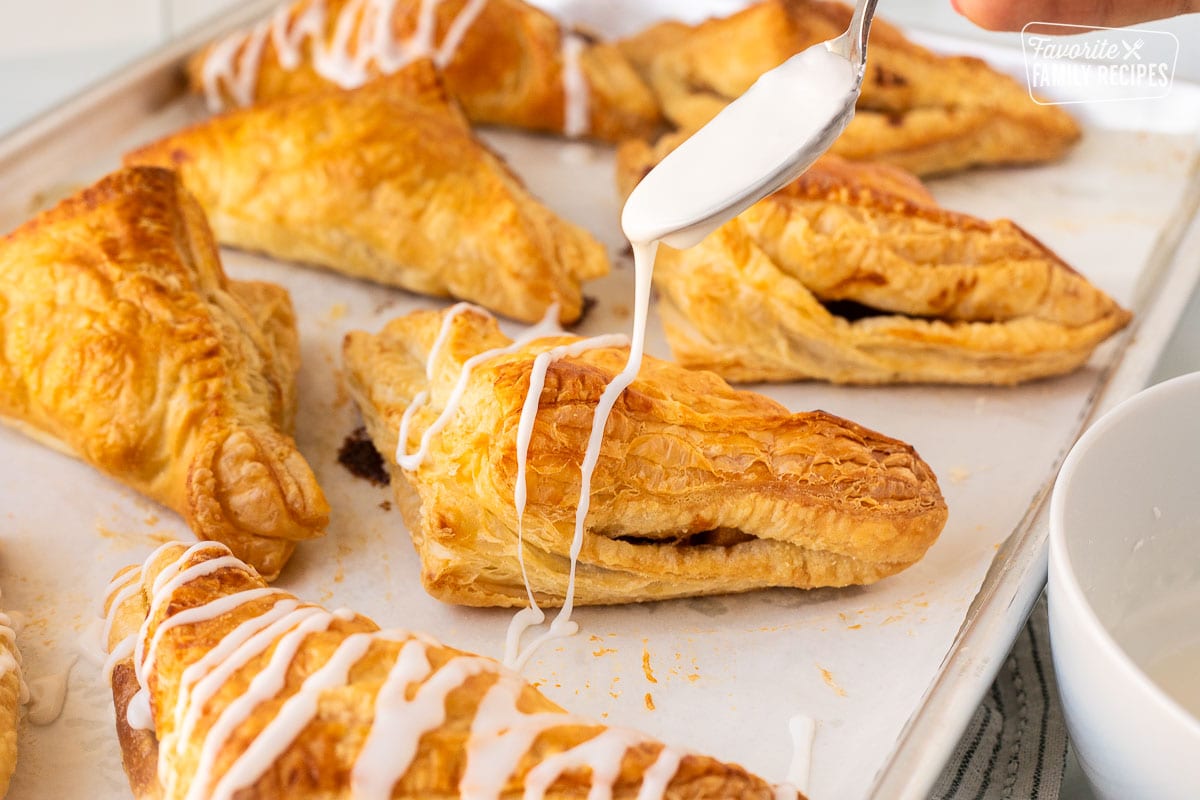 Drizzling white icing over baked apple turnovers.