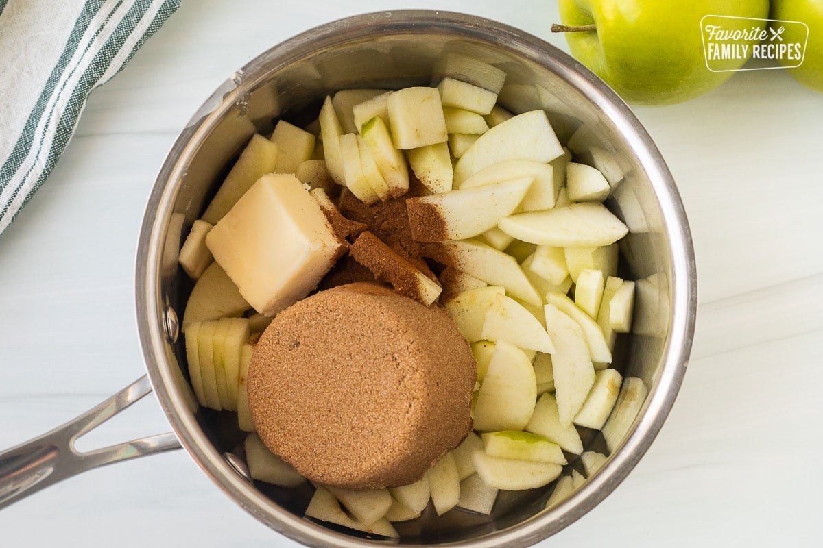 Saucepan with cut apples, butter, apple pie spice and brown sugar.