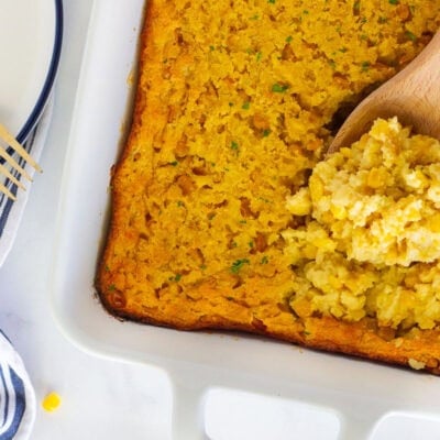 Wooden spoon with scooped corn casserole in a baking dish.