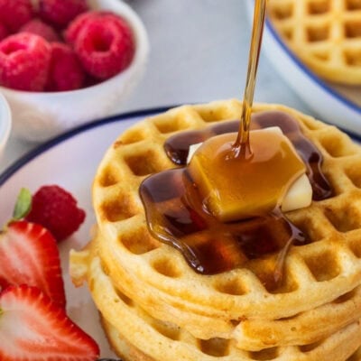 Pouring syrup onto a stack of waffles with a pad of butter.