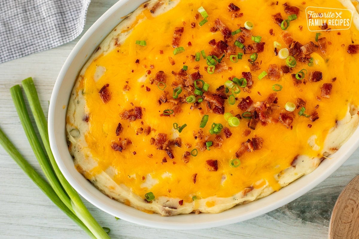 Close up of a baking dish of Loaded Mashed Potatoes garnished with bacon and sliced green onions.