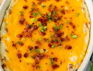 Casserole dish of Loaded Mashed Potatoes garnished with bacon and green onion slices.