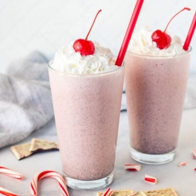 Two glasses of Chick Fil A Peppermint Milkshake topped with whipped cream and a cherry.