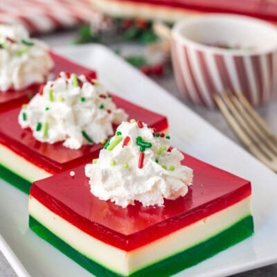 Christmas Jell-O salad slice on a plate with whipped cream and sprinkles.