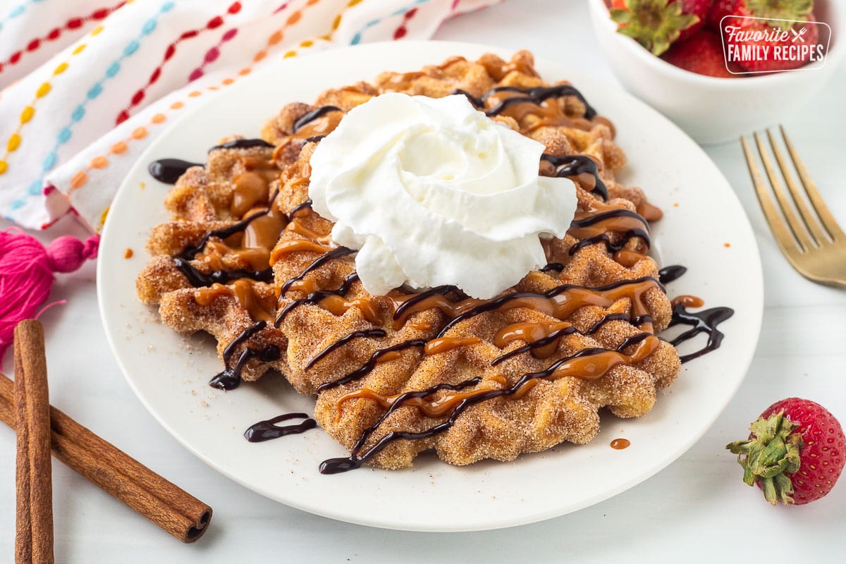 Plate of churro waffles with chocolate and caramel sauce on top and whipped cream.