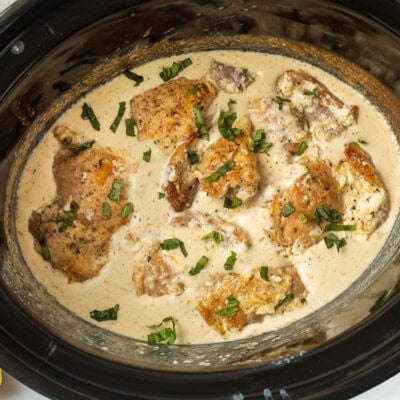 Crockpot with cooked garlic Parmesan chicken and garnished with basil.