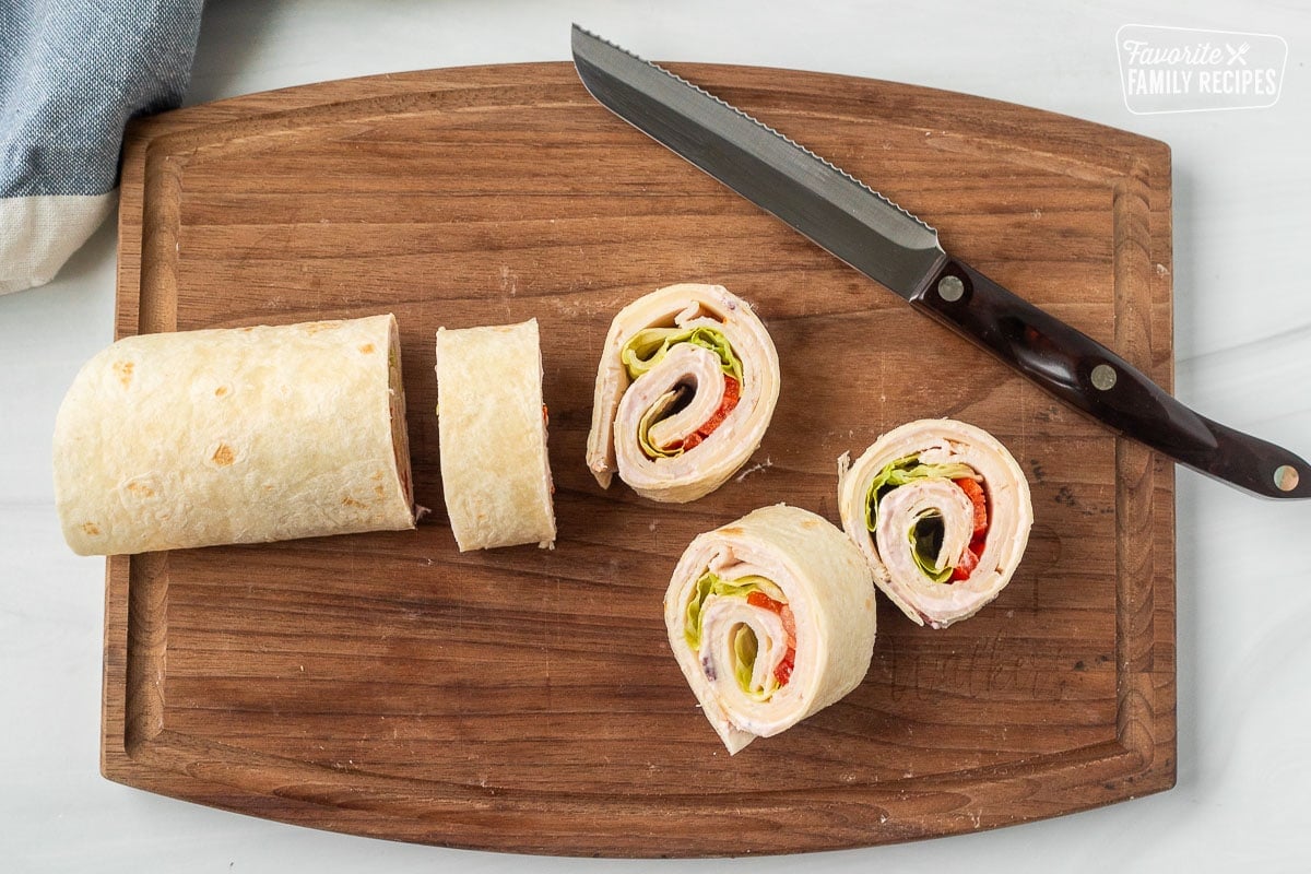 Cutting board with knife and sliced turkey roll ups.