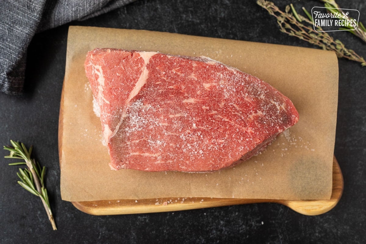 Uncooked beef roast on parchment covered cutting board rubbed with kosher salt.