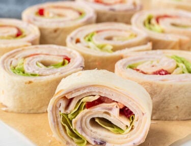 Turkey roll ups on parchment paper filled with cranberry cream cheese, turkey slices, Swiss cheese, tomatoes and lettuce.