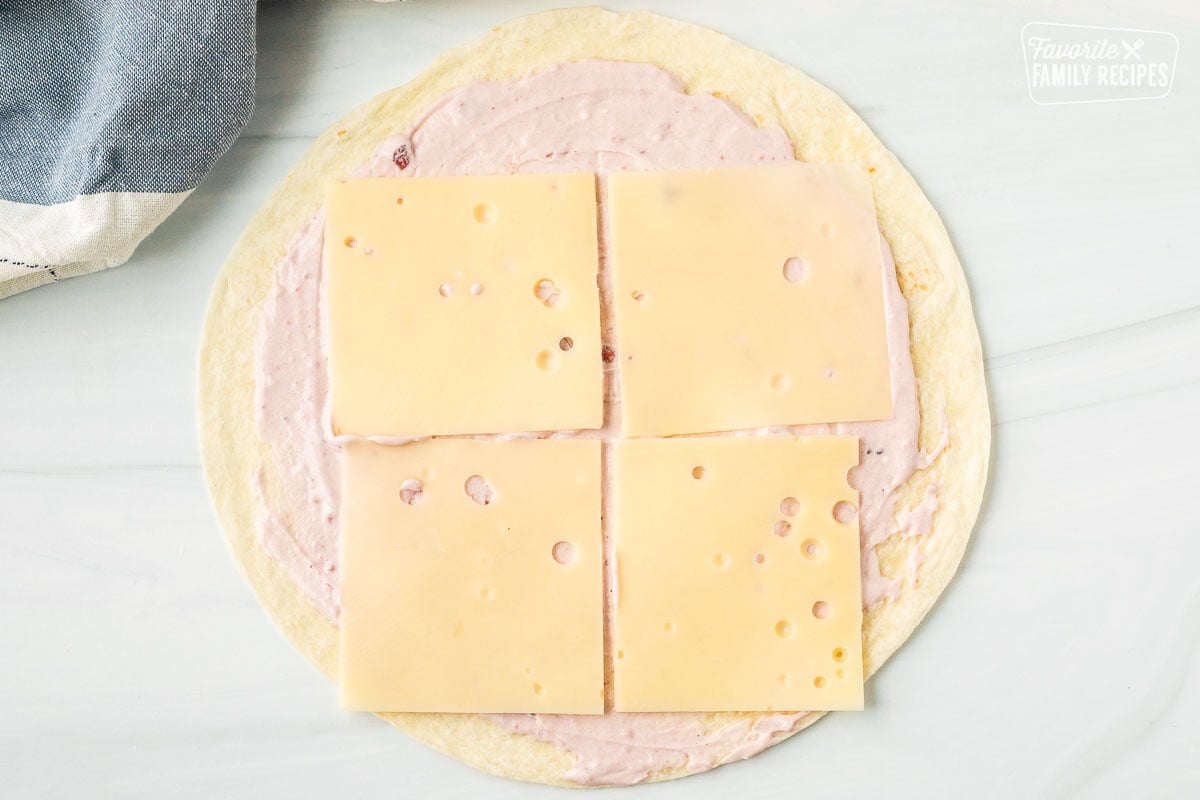 Flour tortilla with cranberry cream cheese spread on top and four slices of Swiss cheese.