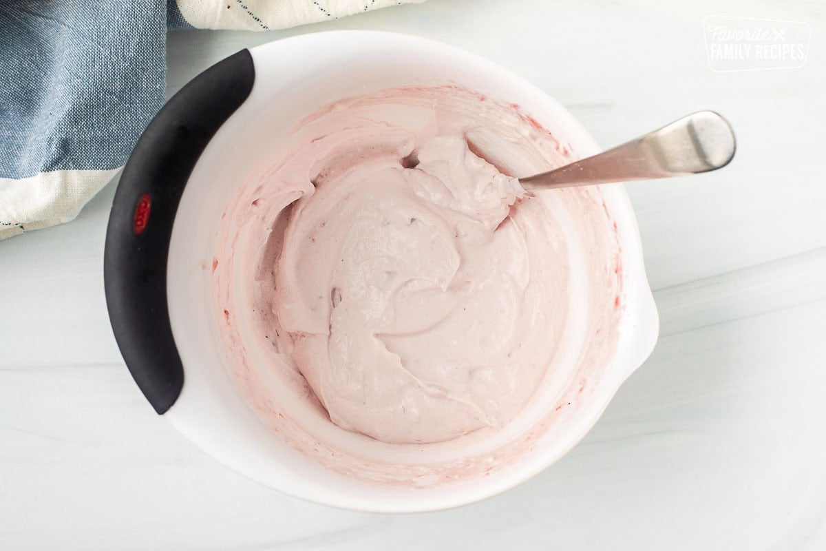 Mixing bowl with cream cheese and cranberry sauce mixed together with a spoon.