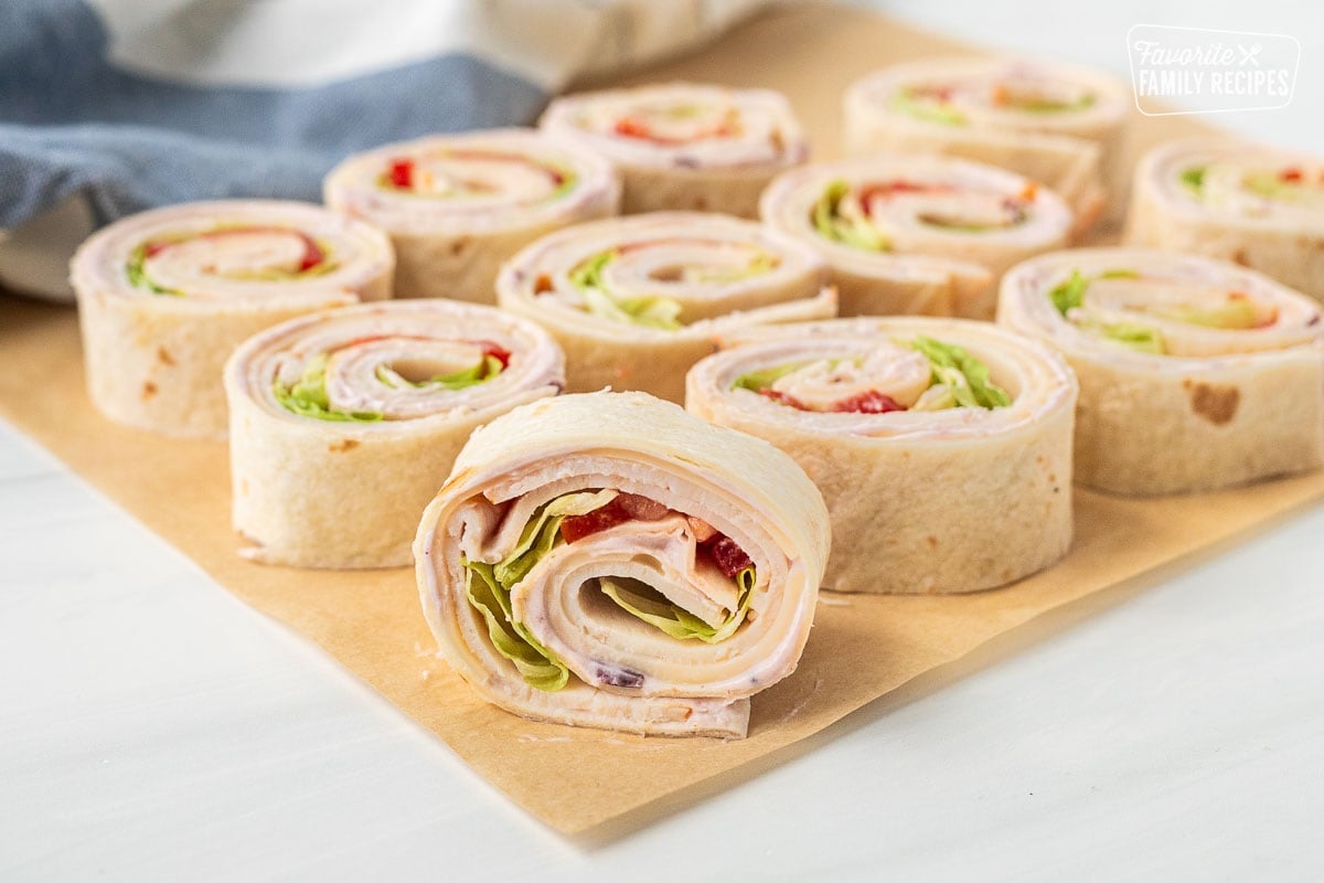 Parchment paper with turkey roll ups on top filled with cranberry cream cheese, turkey slices, Swiss cheese, tomatoes and lettuce.