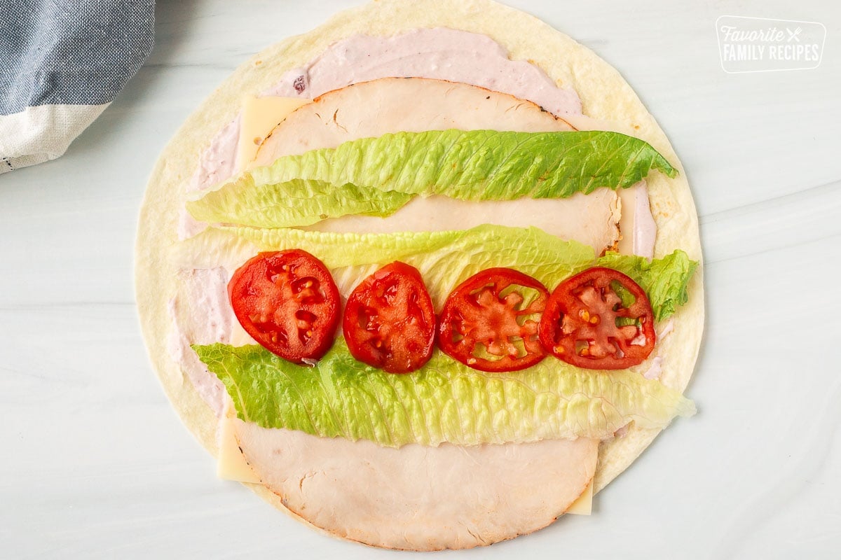 Tortilla with cranberry cream cheese spread on top with a layer of Swiss cheese, turkey slices, lettuce and tomatoes.