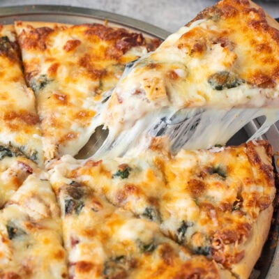 Lifting a slice of Alfredo pizza with the cheese pulling from the sides.