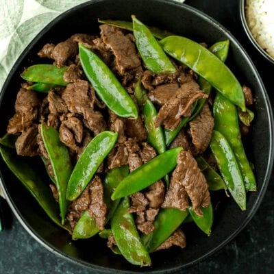 Beef with snow peas in a serving bowl next to a small bowl of rice