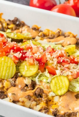 Casserole dish of Big Mac Casserole topped with pickles, lettuce, tomatoes and onions.
