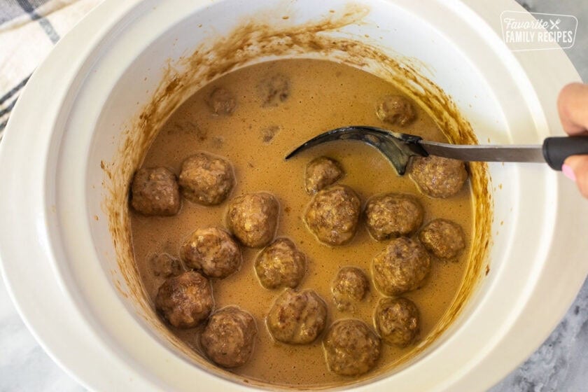 Stirring Crock Pot Swedish Meatballs with a spoon.