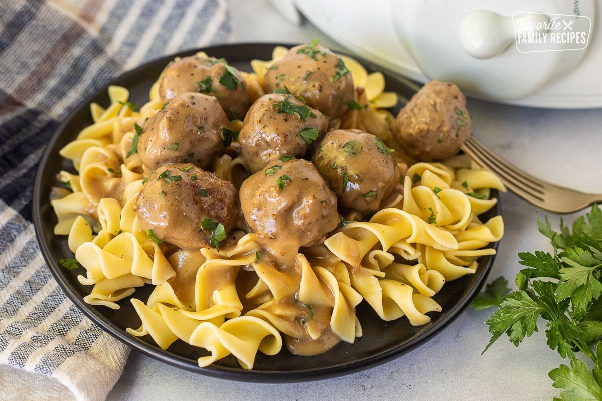 Crock Pot Swedish Meatballs over noodles on a plate garnished with parsley.