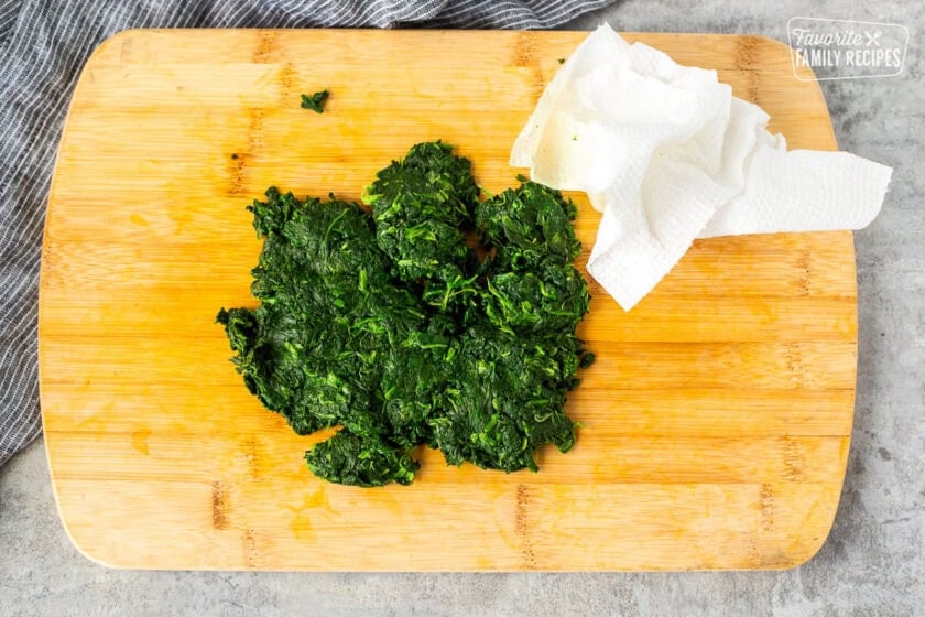 Cutting board with squeezed out spinach and a paper towel.