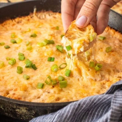 Dipping a slice of bread into a skillet of Hot Crab Dip.