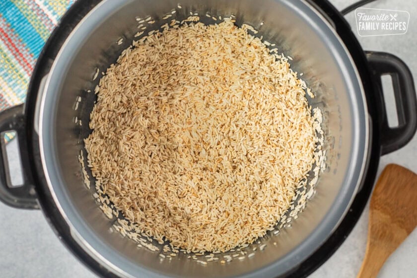 Instant pot with golden brown rice and a wooden spoon on the side.