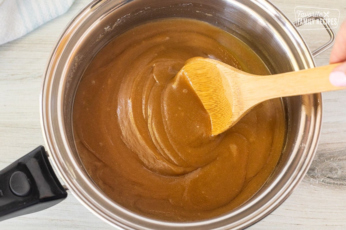 Saucepan with brown sugar butter mixture and a wooden spoon stirring.