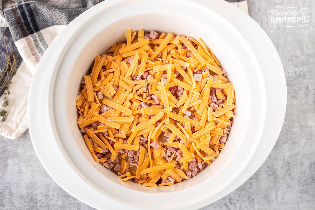 Crockpot with layer of potatoes and ham cubes and shredded cheddar cheese.