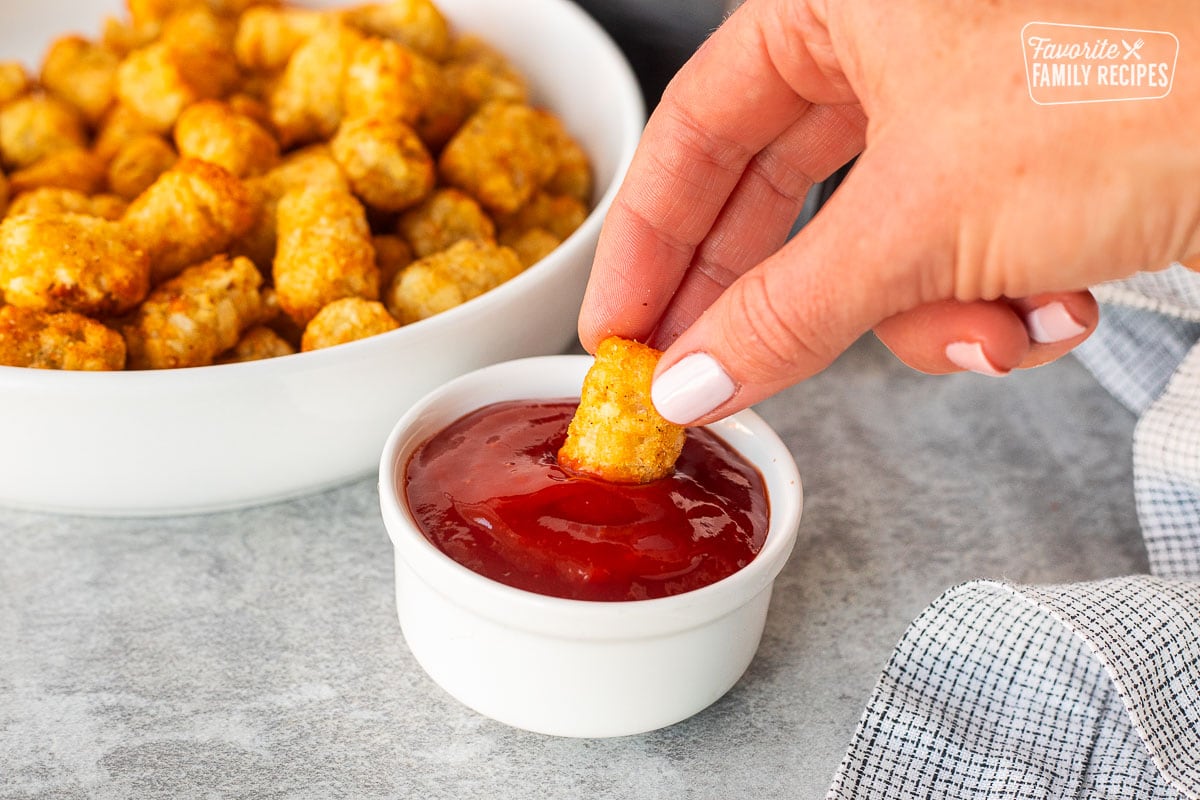 Hand dipping an Air Fryer Tater Tot into ketchup.