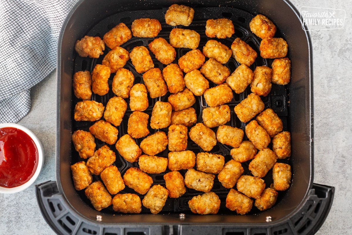 Single layer of Tater Tots in the Air Fryer with a cup of ketchup on the side.