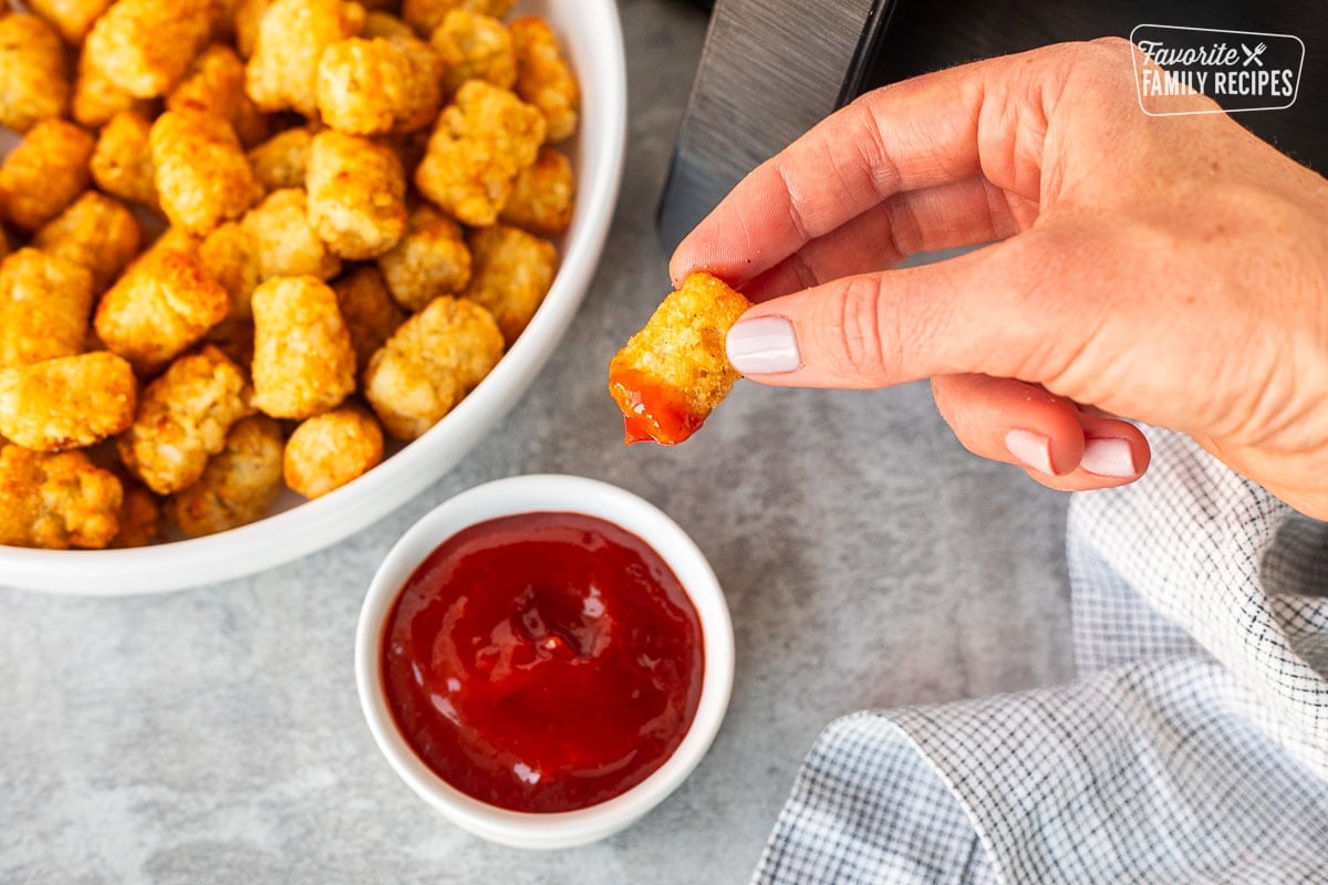 Hand holding an Air Fryer Tater Tot that has been dipped into a cup of ketchup.