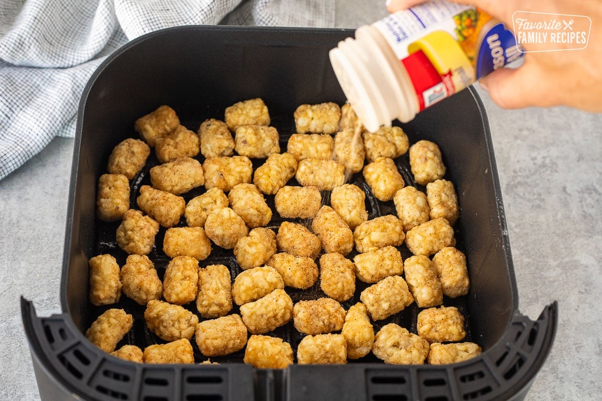 Shaking seasoning salt on top of Frozen Tater Tots in the Air Fryer basket.