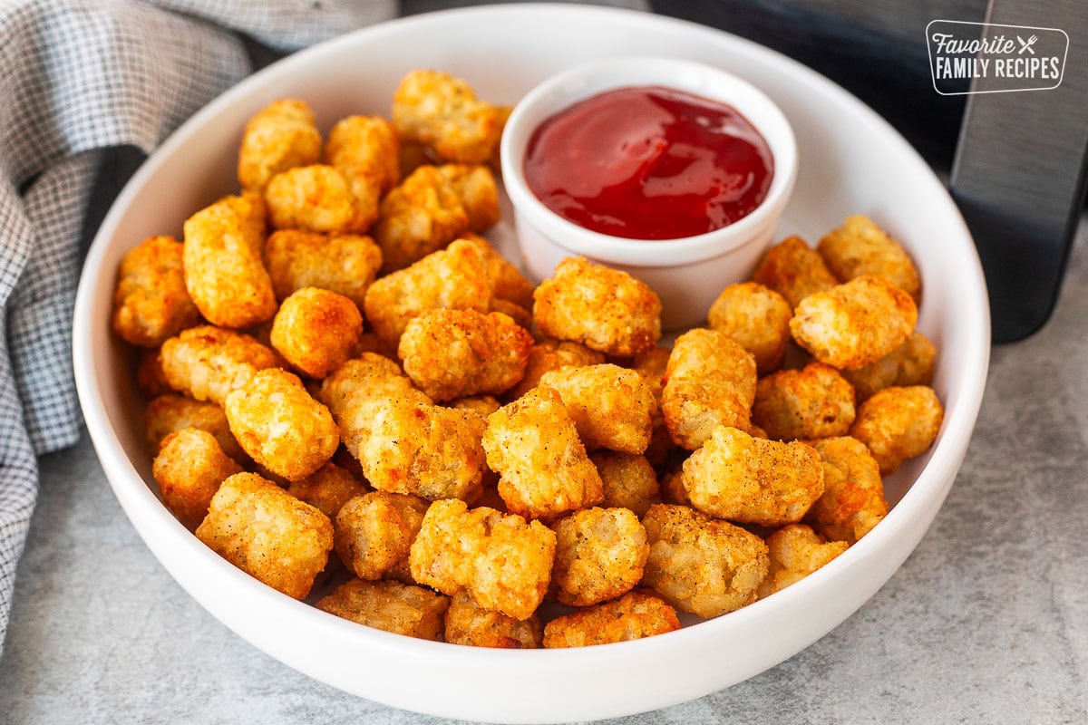 Plate of golden Tater Tots next to Air Fryer basket and a cup of ketchup.
