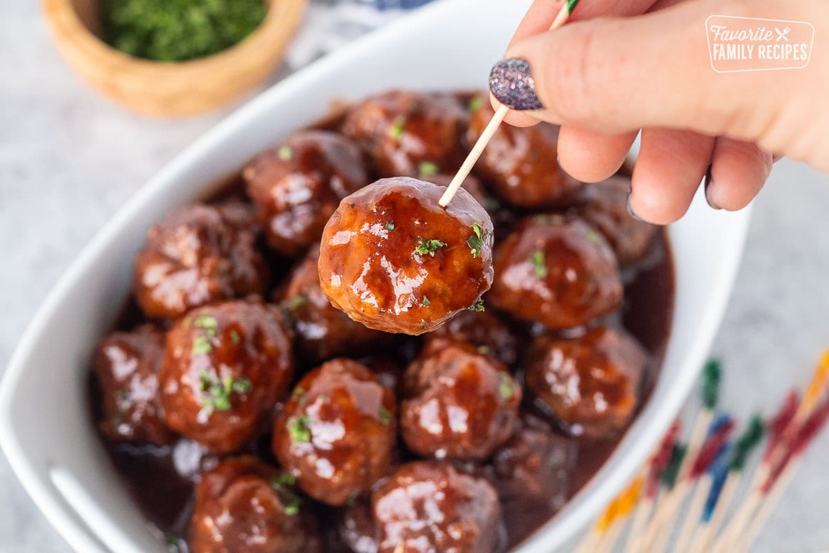 Grape jelly meatballs garnished with fresh parsley stabbed with a toothpick.