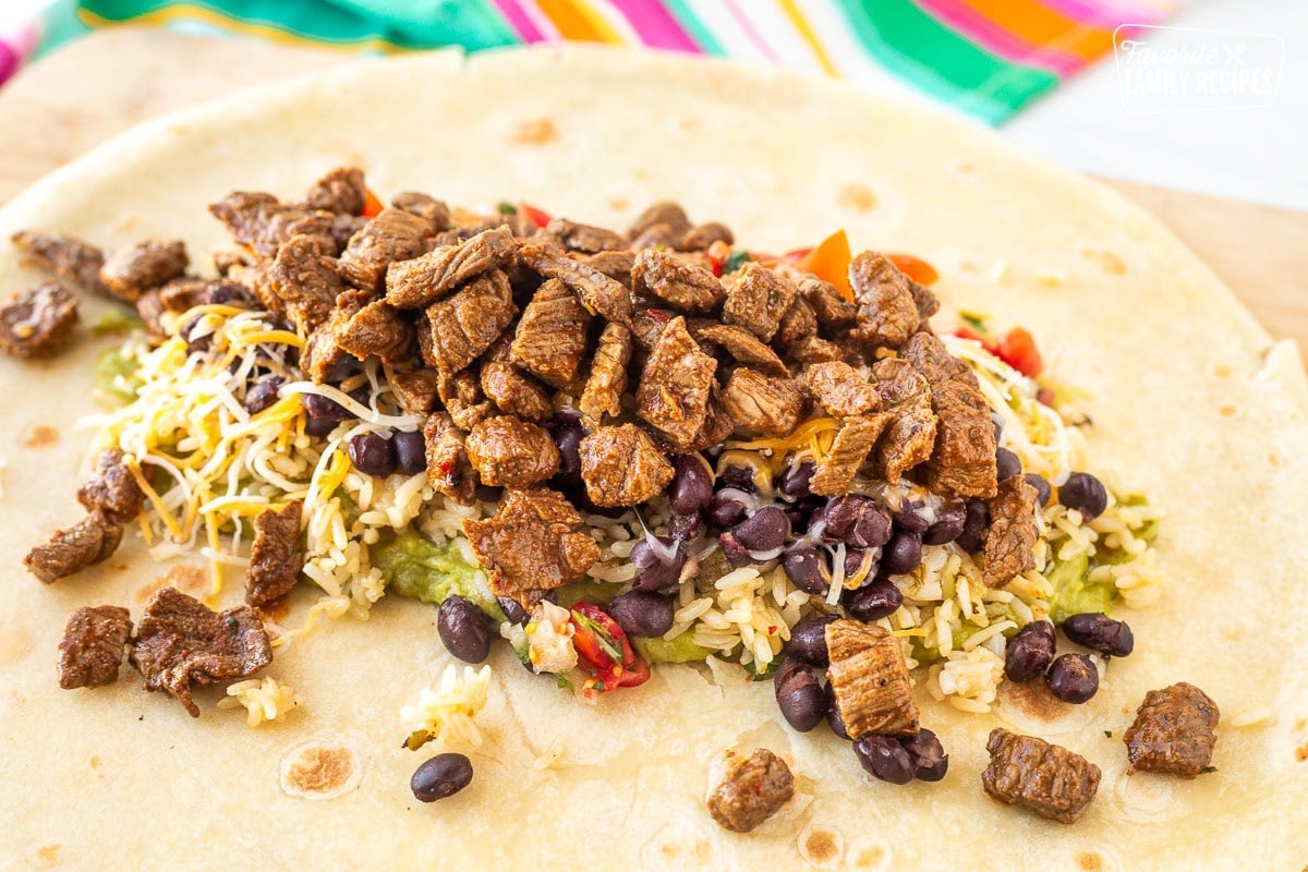 Close up of topping on the flour tortilla including guacamole, cilantro lime rice, Black beans, pico de gallo, shredded cheddar cheese and cut up Carne Asada.